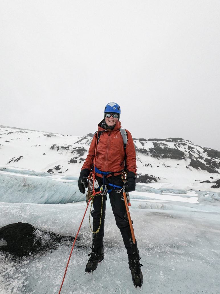Signe Hillerup larsen iført klatreudstyr og sikkerhedsbriller står på sne og is i Island og kigger mod kameraet. Man ser hende forfra i fuld figur.