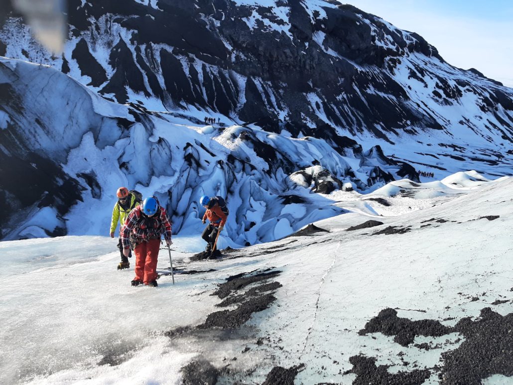Tre mennesker iført klatreudstyr er på vej ned ad en gletsjer. De står foroverbøjede.