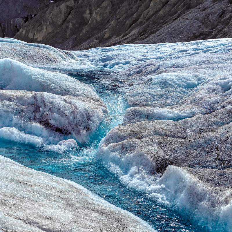 Nærbillede af blåt smeltevand, der strømmer gennem is. 
